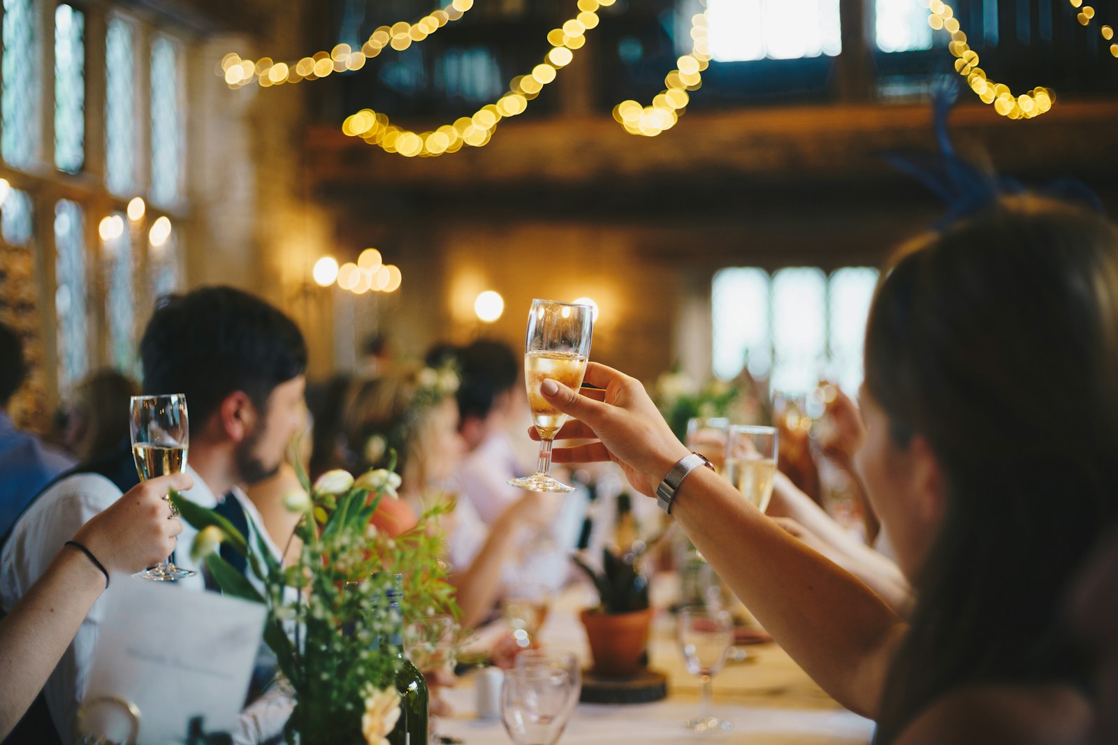 Guests raising champagne flutes across candlelit reception dining table with fairy lights